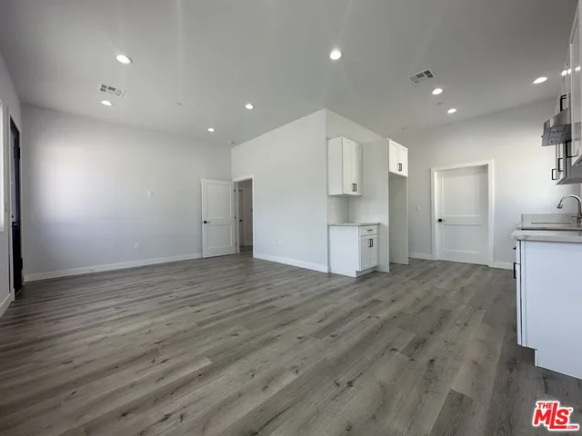 a view of empty room with wooden floor and kitchen