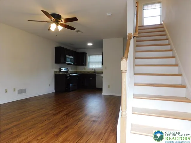 a view of an empty room with wooden floor and a kitchen
