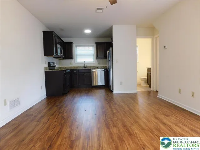 a kitchen with stainless steel appliances granite countertop a refrigerator a stove top oven a sink and dishwasher with wooden floor