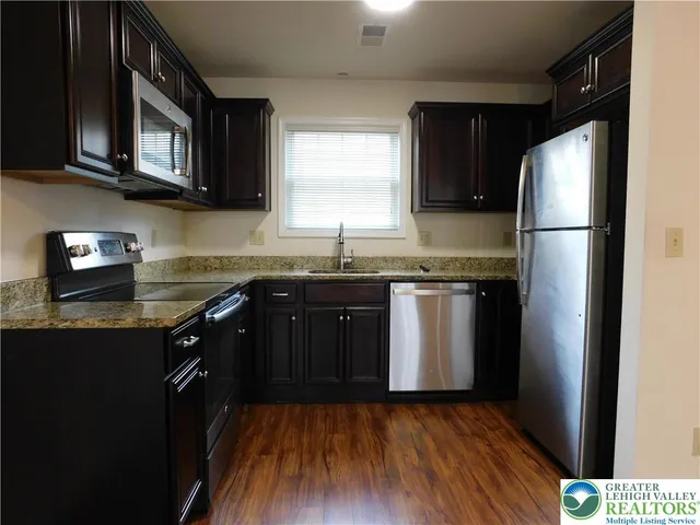 a kitchen with stainless steel appliances granite countertop a stove a refrigerator a sink dishwasher and wooden cabinets with wooden floor