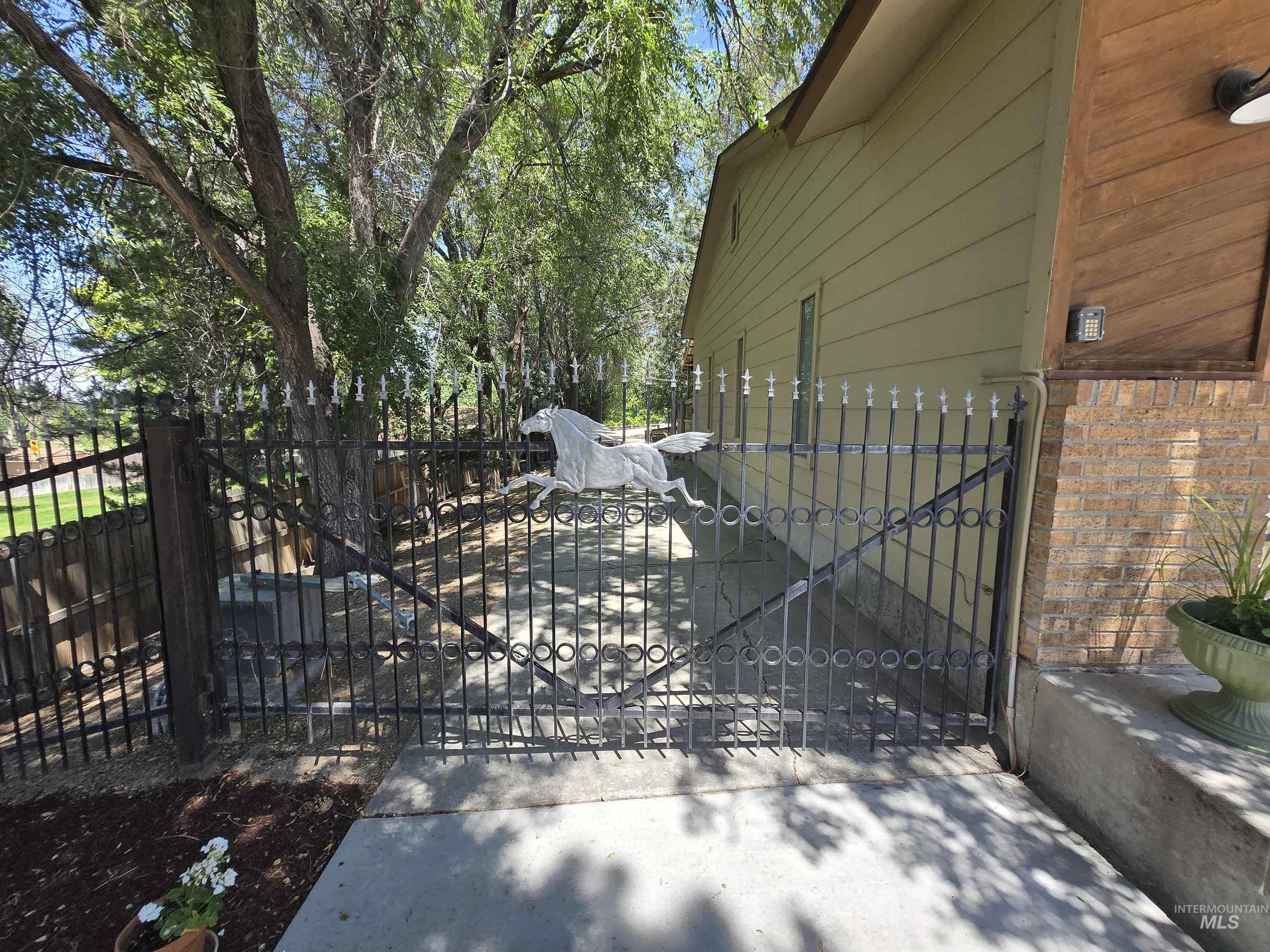 12050 West Hidden Valley Rim Road Boise, ID 83709 - Photo 21 of 39 Decorative wrought iron gate featuring a horse motif, bordered by mature trees and a concrete walkway
