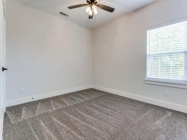 an empty room with a chandelier fan and windows
