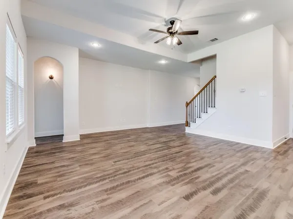 a view of an empty room with wooden floor and a ceiling fan