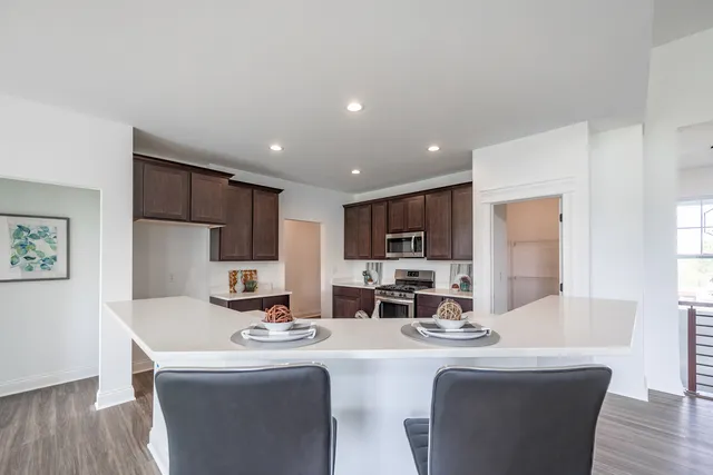 a dining hall with stainless steel appliances granite countertop a sink a stove a dining table and chairs with wooden floor