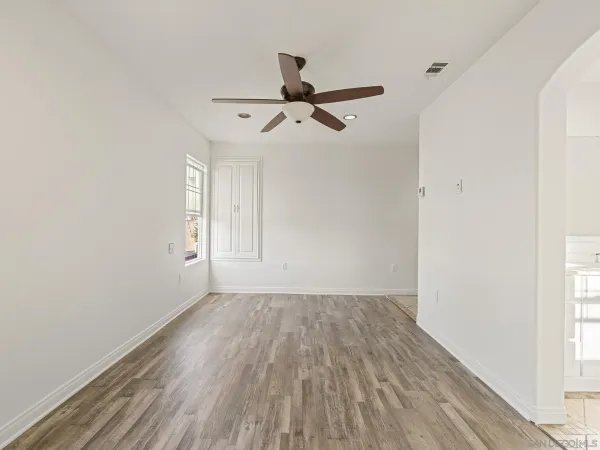 an empty room with wooden floor a ceiling fan and windows