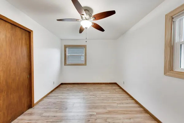 an empty room with wooden floor chandelier fan and windows