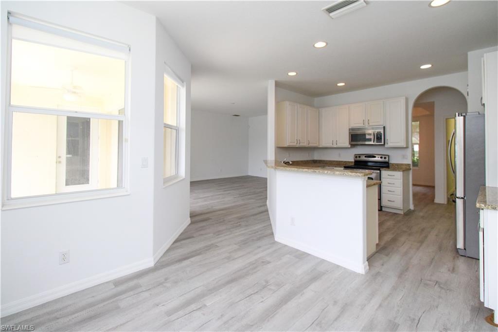 3927 Aurora Court Naples, FL 34116 - Photo 12 of 26 Kitchen featuring arched walkways, light stone countertops, stainless steel appliances, white cabinetry, and recessed lighting
