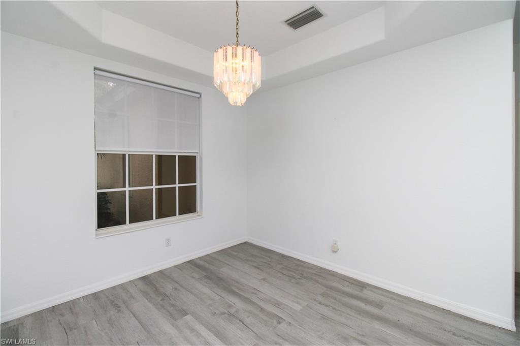 3927 Aurora Court Naples, FL 34116 - Photo 15 of 26 Unfurnished room with a raised ceiling, wood finished floors, and a chandelier