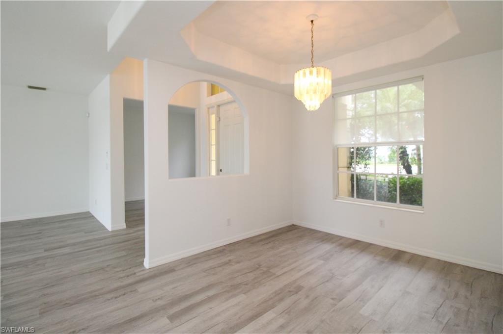 3927 Aurora Court Naples, FL 34116 - Photo 4 of 26 Unfurnished room with a chandelier, light wood-type flooring, and a raised ceiling