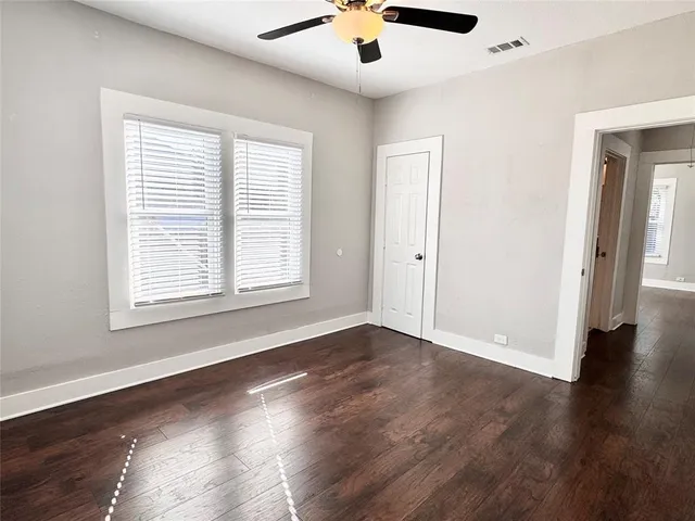 an empty room with wooden floor chandelier fan and windows