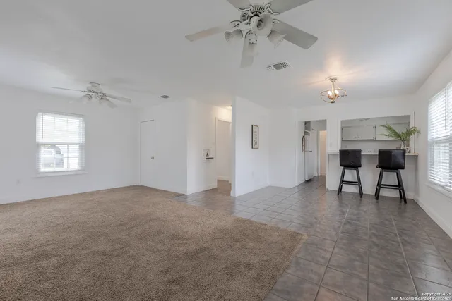 an empty room with chandelier fan and windows
