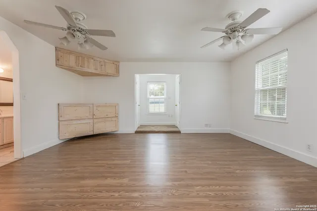 an empty room with wooden floor chandelier fan and windows