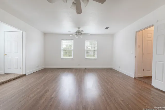 an empty room with wooden floor chandelier fan and windows