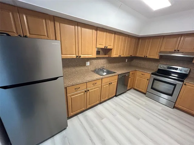 a kitchen with stainless steel appliances granite countertop a refrigerator a sink dishwasher a stove with wooden cabinets and floors