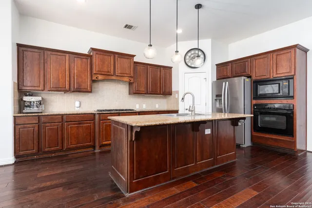 a kitchen with stainless steel appliances granite countertop wooden cabinets a stove a sink and dishwasher with wooden floor