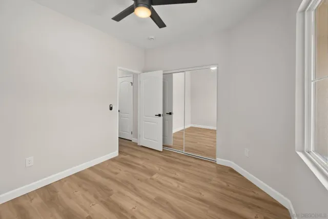 an empty room with wooden floor fan and windows