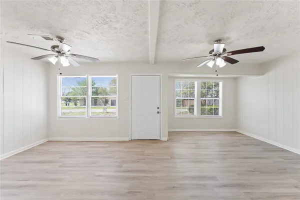 an empty room with wooden floor chandelier fan and windows