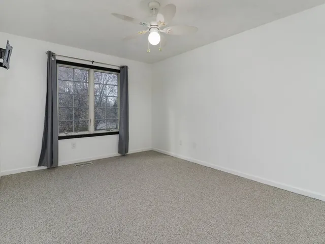 an empty room with chandelier fan and windows