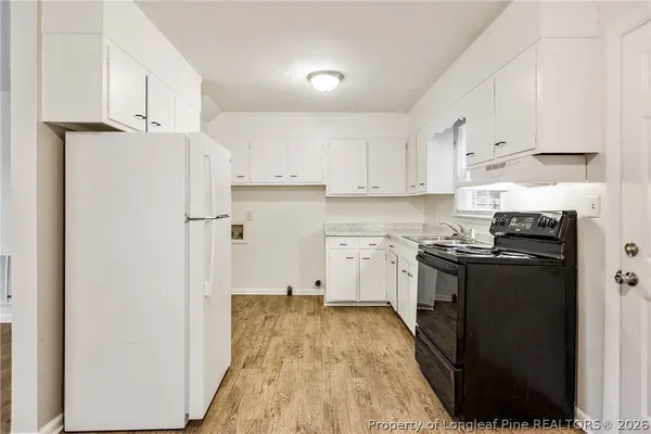 a kitchen with a refrigerator a stove top oven and white cabinets