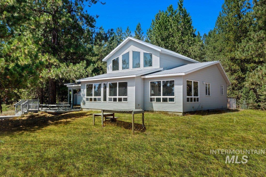 Rear view of house featuring a metal roof, a deck, a yard, and view of wooded area