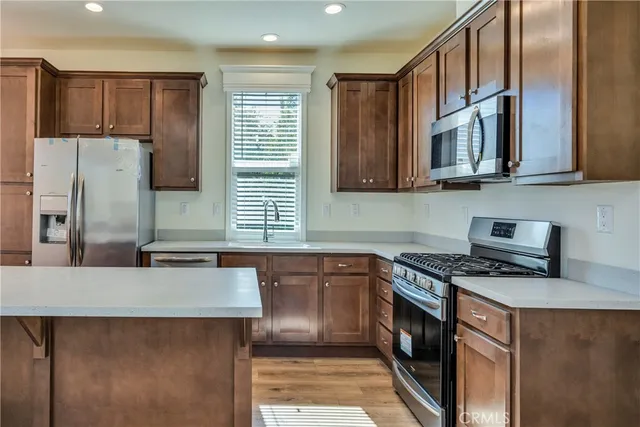 a kitchen with stainless steel appliances granite countertop a stove a sink dishwasher and a refrigerator with wooden cabinets