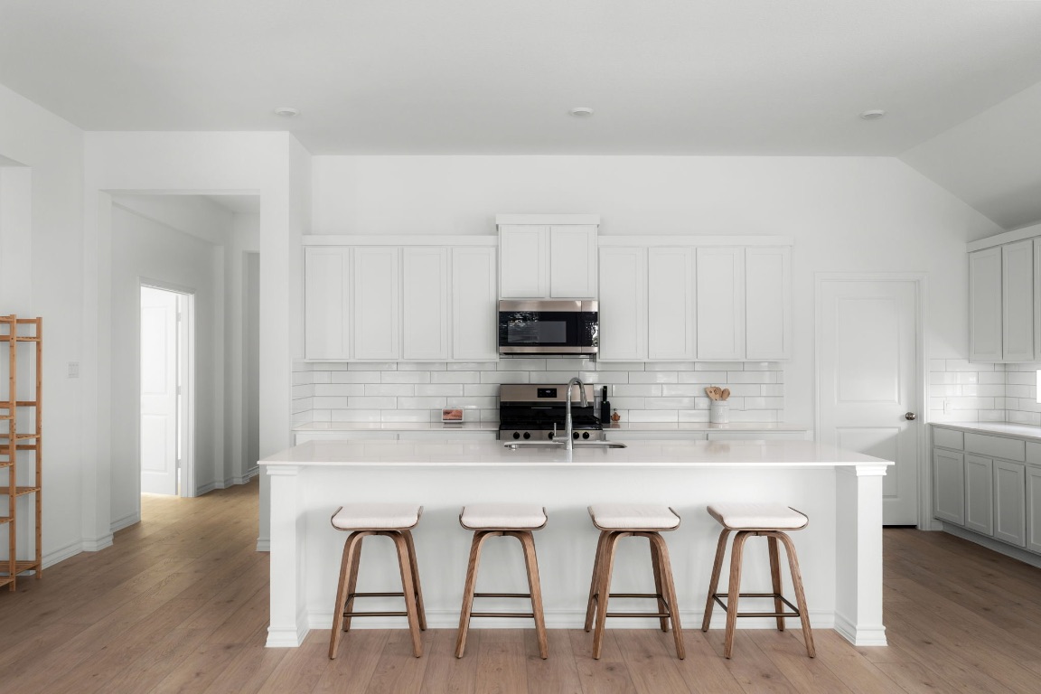 4264 Hill House Lane Georgetown, TX 78628 - Photo 7 of 30 Kitchen with a kitchen breakfast bar, a center island with sink, decorative backsplash, stainless steel appliances, and white cabinetry