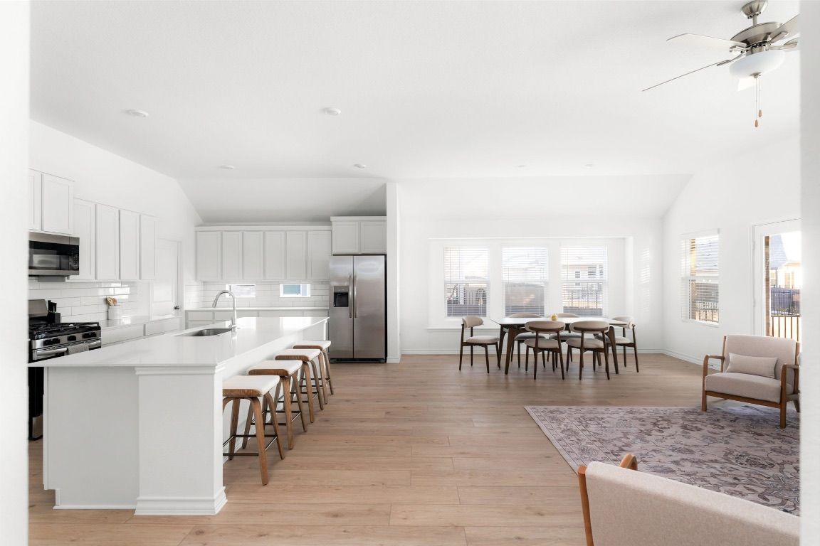 4264 Hill House Lane Georgetown, TX 78628 - Photo 9 of 30 Kitchen with lofted ceiling, appliances with stainless steel finishes, a breakfast bar area, a kitchen island with sink, and light wood-style floors