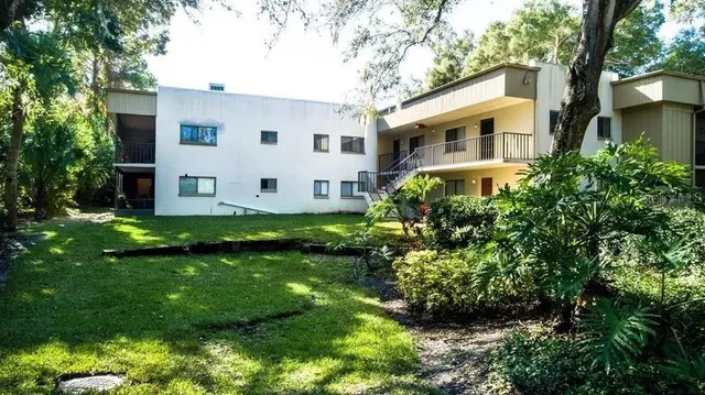 a view of a white house with a big yard plants and large trees