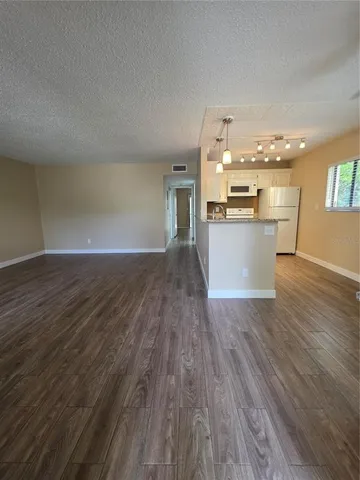 a view of an empty room and kitchen with wooden floor