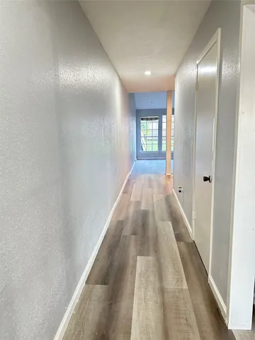 a view of a hallway with wooden floor and a bathroom
