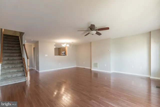 a view of an empty room with wooden floor and a ceiling fan