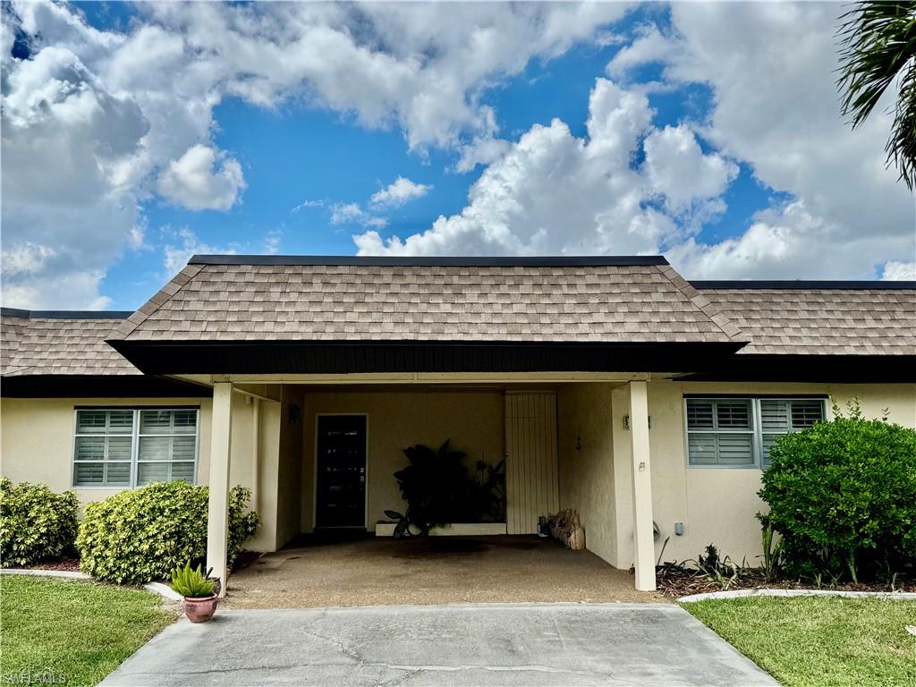 View of front of house featuring stucco siding, roof with shingles, an attached carport, and a front yard