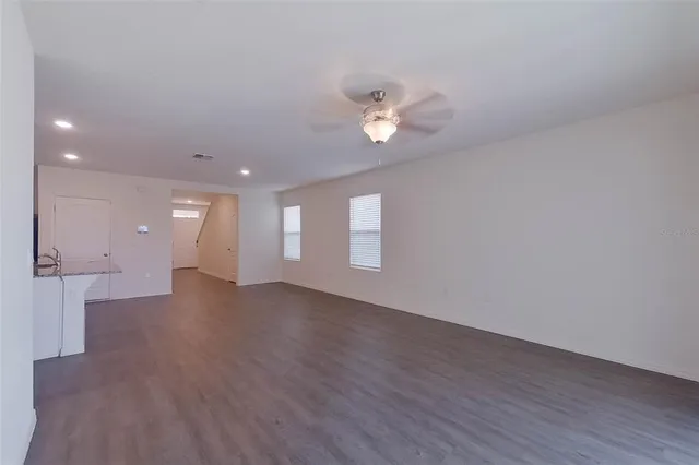 a view of an empty room with wooden floor and a ceiling fan