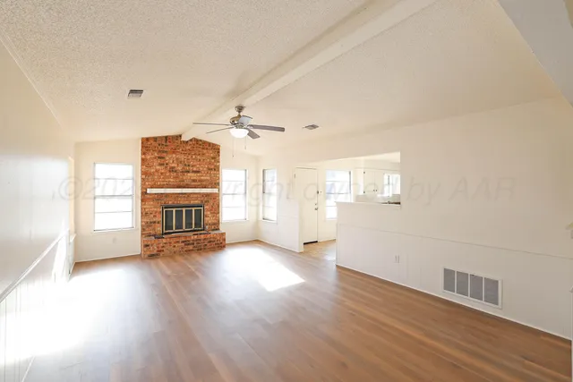 an empty room with wooden floor fireplace and windows