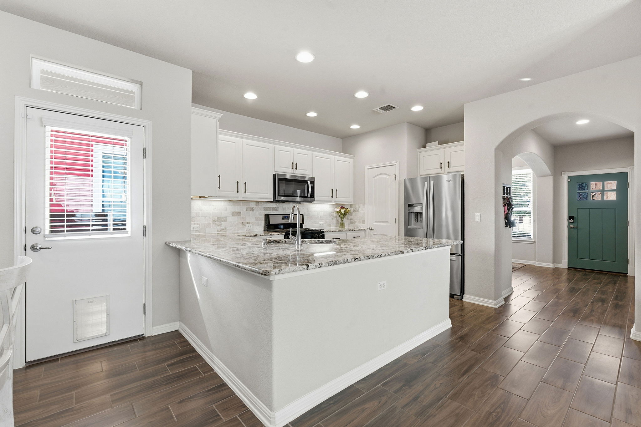 6005 Baythorne Drive Austin, TX 78747 - Photo 7 of 40 Kitchen with a peninsula, wood tiled floors, white cabinetry, light stone countertops, and arched walkways