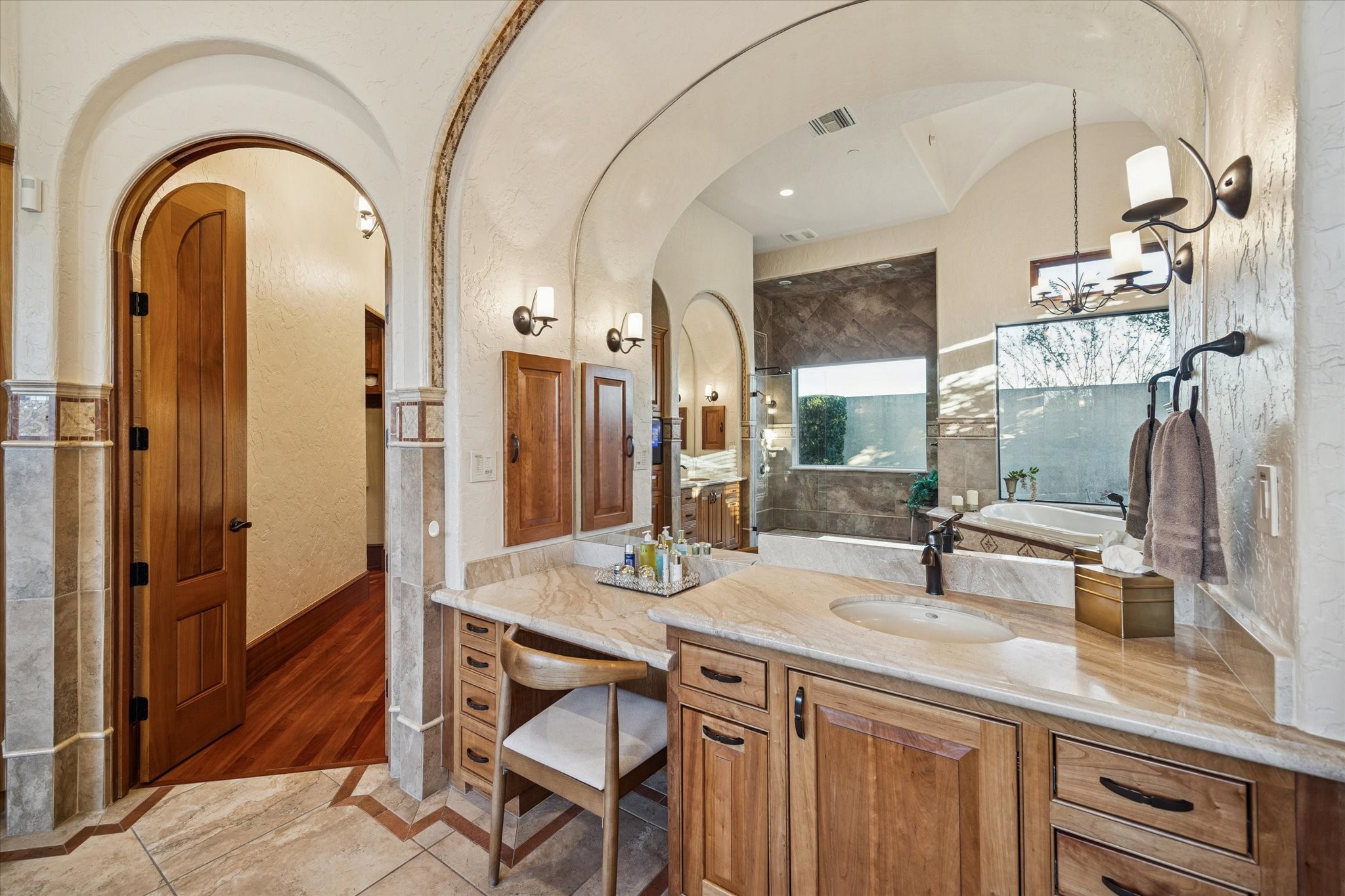 21538 Mueschke Road Tomball, TX 77377 - Photo 19 of 50 Primary bathroom details. This beautifully designed space showcases custom cabinetry with organized drawer systems, a majestic arched mirror highlighting the Mediterranean style, and granite countertops with wood accents. Every element, from the colors to the finishes, invites calm and serenity, providing the perfect setting to prepare for your day or unwind in peaceful luxury, helping you feel your absolute best.