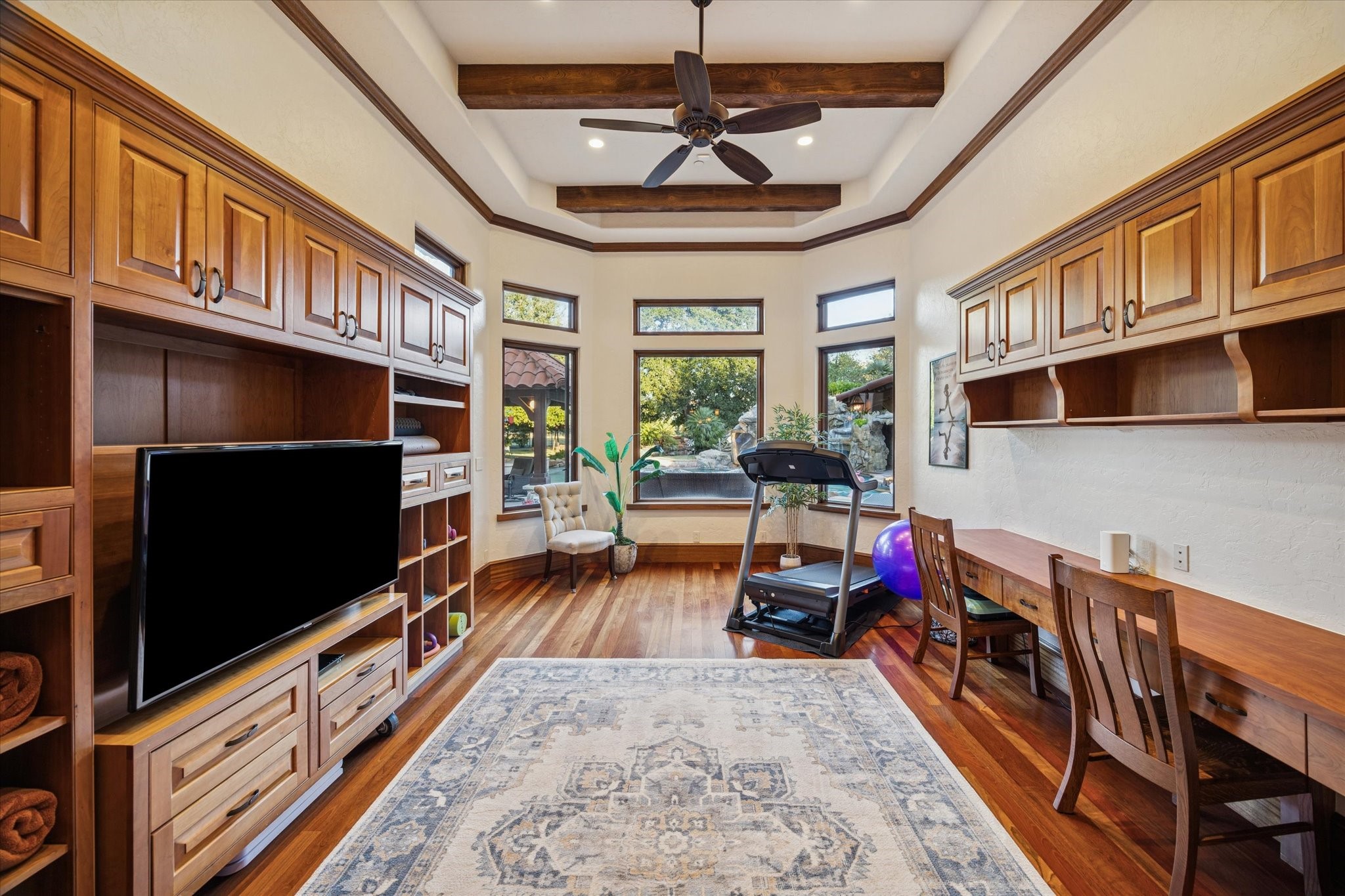 21538 Mueschke Road Tomball, TX 77377 - Photo 22 of 50 A space where inspiration and serenity meet. This elegant flex room, filled with natural light and framed by grand windows overlooking the pool, features a tray ceiling with wood beams and custom cabinetry. Perfect as a gym, game room, or sophisticated home-schooling area with a built-in desk and upper storage cabinets, an inspiring setting for productivity and calm.