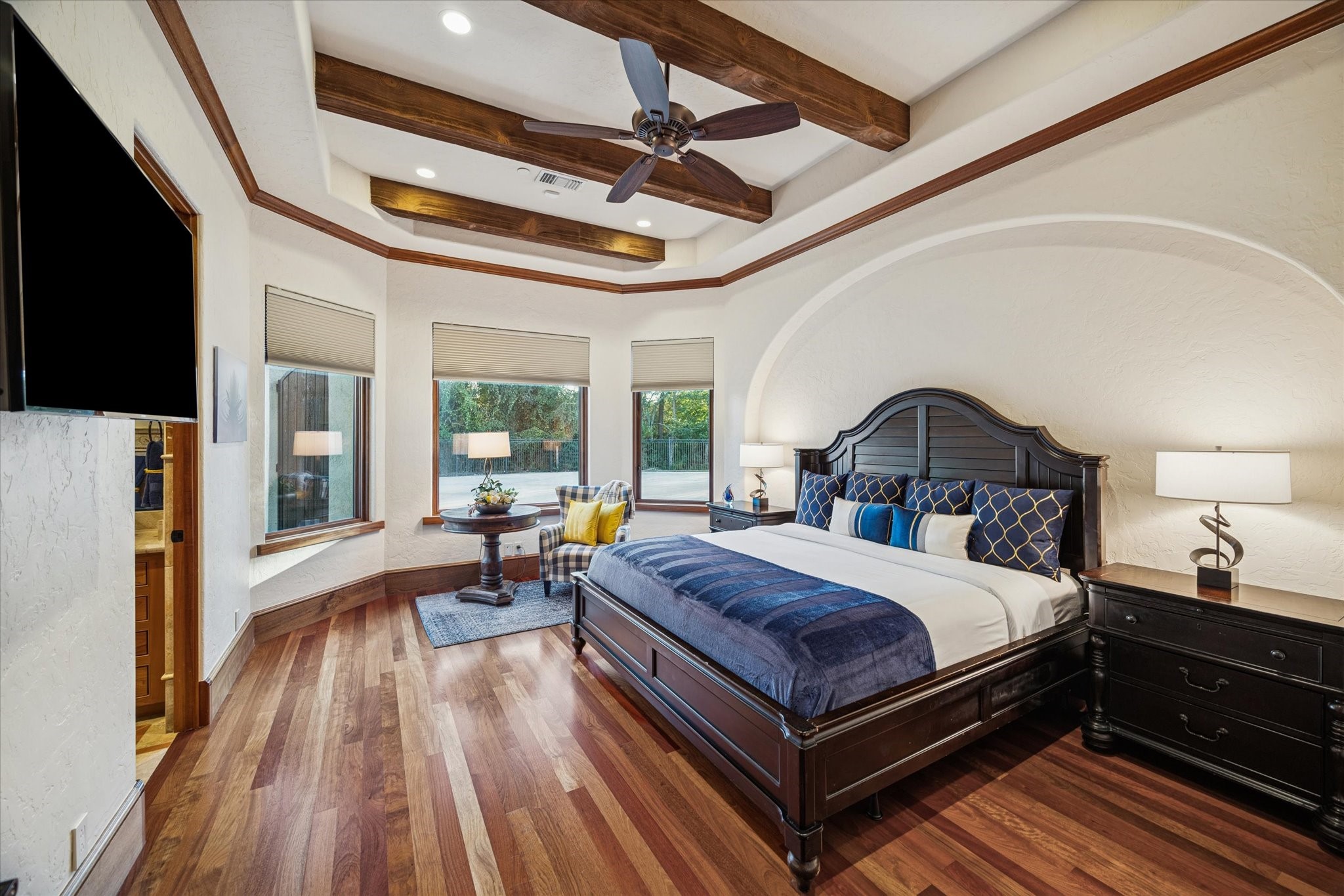 21538 Mueschke Road Tomball, TX 77377 - Photo 25 of 50 Spacious secondary bedroom featuring a beautiful arch and wall of windows that fill the room with natural light. Refined wood elements and rustic wood beams over the tray ceiling evoke the warmth and charm of a Mediterranean hacienda. The room also includes a private en-suite bathroom, offering added privacy and convenience, an inviting and elegant retreat your loved ones will adore.