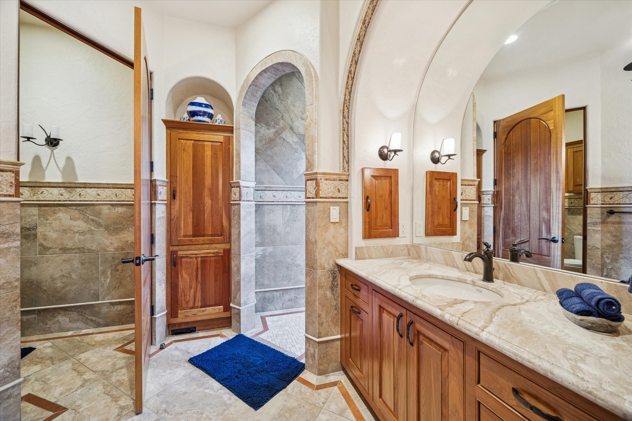 21538 Mueschke Road Tomball, TX 77377 - Photo 26 of 50 Elegant en-suite bathroom seamlessly connected to the bedroom, showcasing exquisite finishes and thoughtful design. The spacious vanity with a beautiful countertop provides comfort and functionality, while the combination of stone and tile flooring in warm earthy tones creates a serene and refined ambiance, simply exceptional.