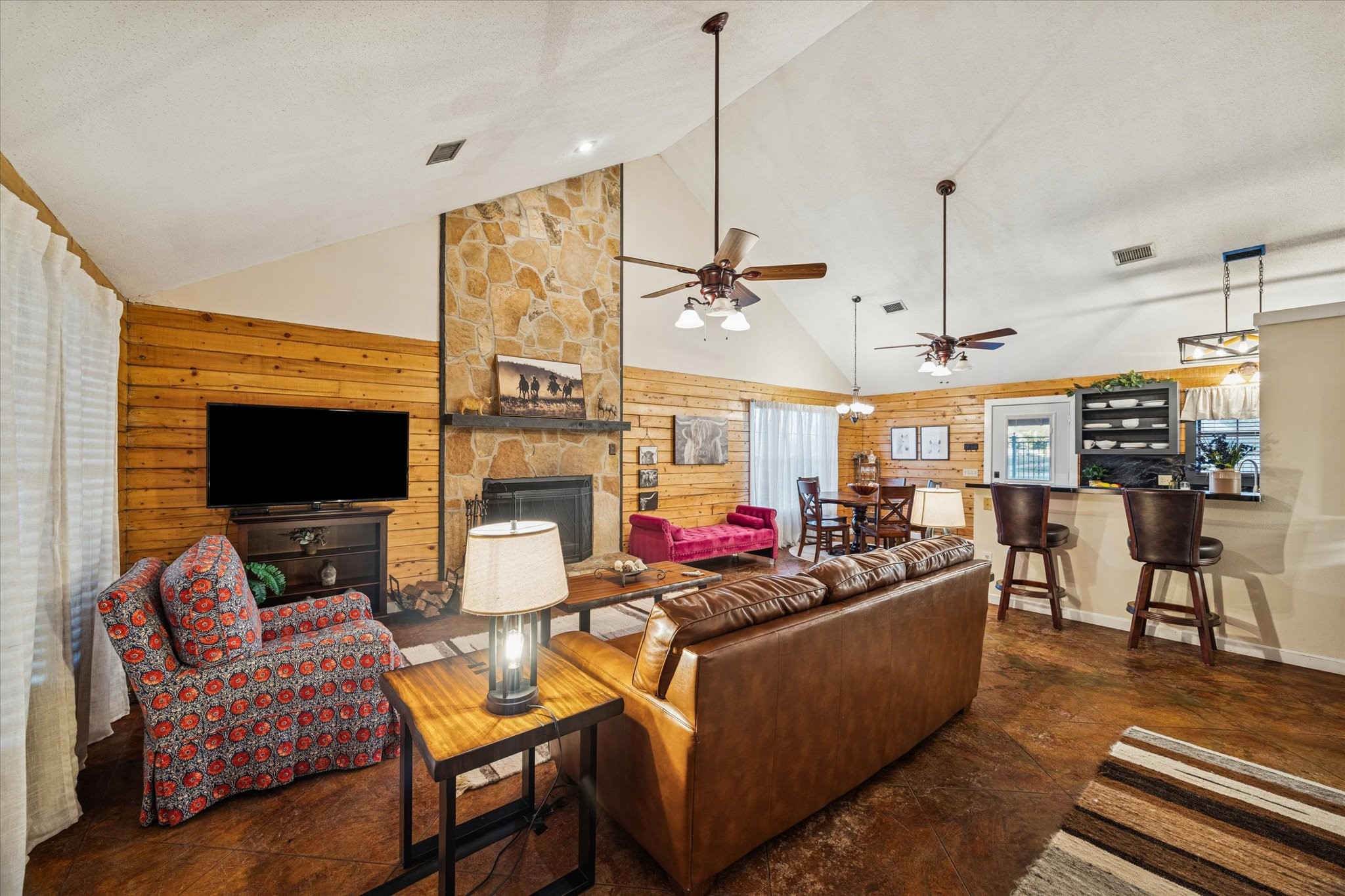 21538 Mueschke Road Tomball, TX 77377 - Photo 38 of 50 Inside, the cabin showcases timeless wood finishes and cozy textures that highlight its natural character. The living area features soaring vaulted ceilings, a striking stone fireplace, and open sightlines to the dining and kitchen spaces, perfect for entertaining or family gatherings.