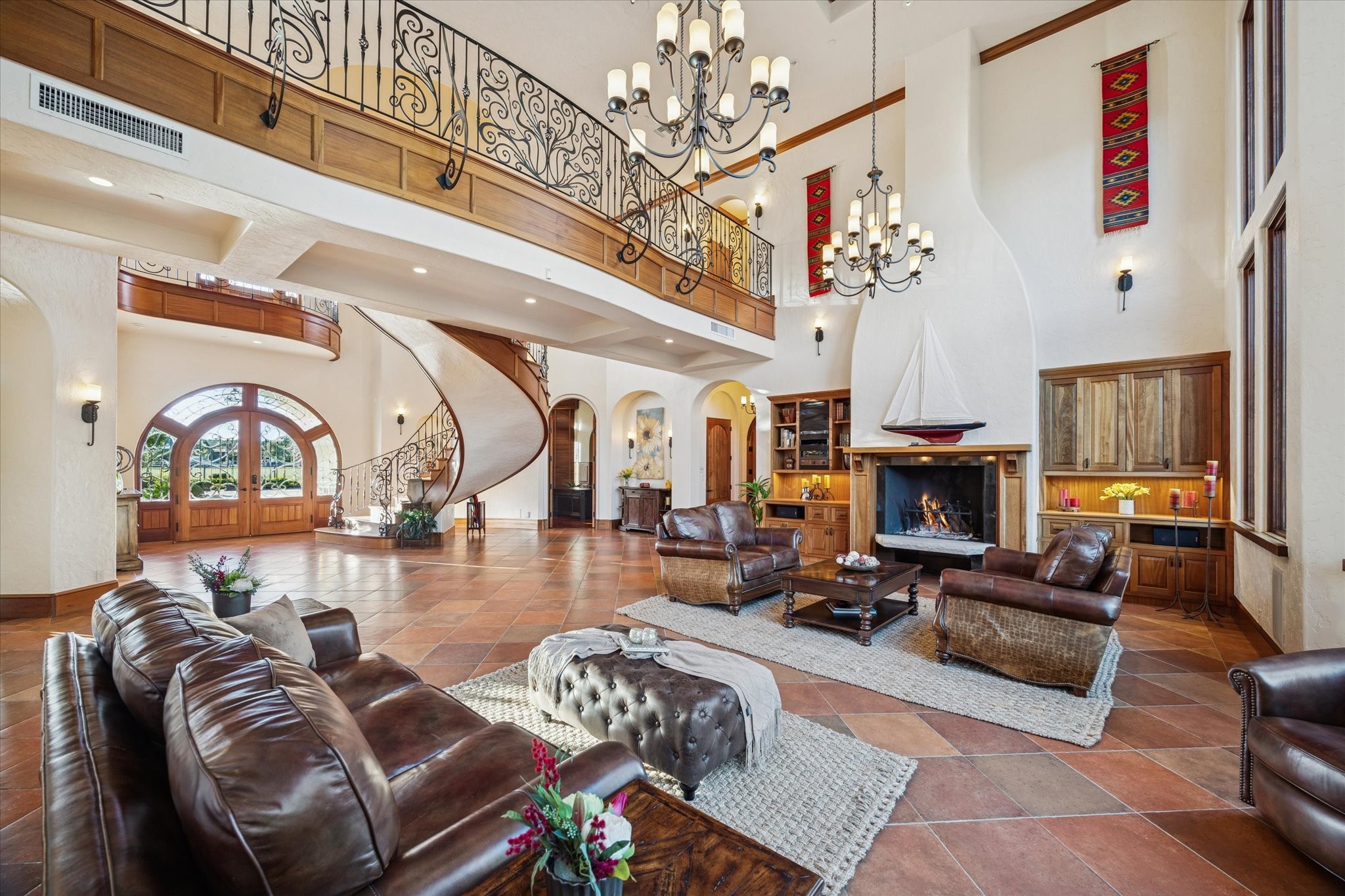 21538 Mueschke Road Tomball, TX 77377 - Photo 4 of 50 Stunning view of the living area and grand foyer. This angle highlights the open, airy layout with the striking staircase and upper-level balcony, filled with natural light. Mediterranean touches include arched niches, doorways, soaring 26-foot ceilings, and a single solid wood staircase with a custom wrought-iron railing crafted as one piece. Saltillo tile floors and richly stained mahogany wood enhance the Hacienda-Mediterranean elegance of this exceptional home.