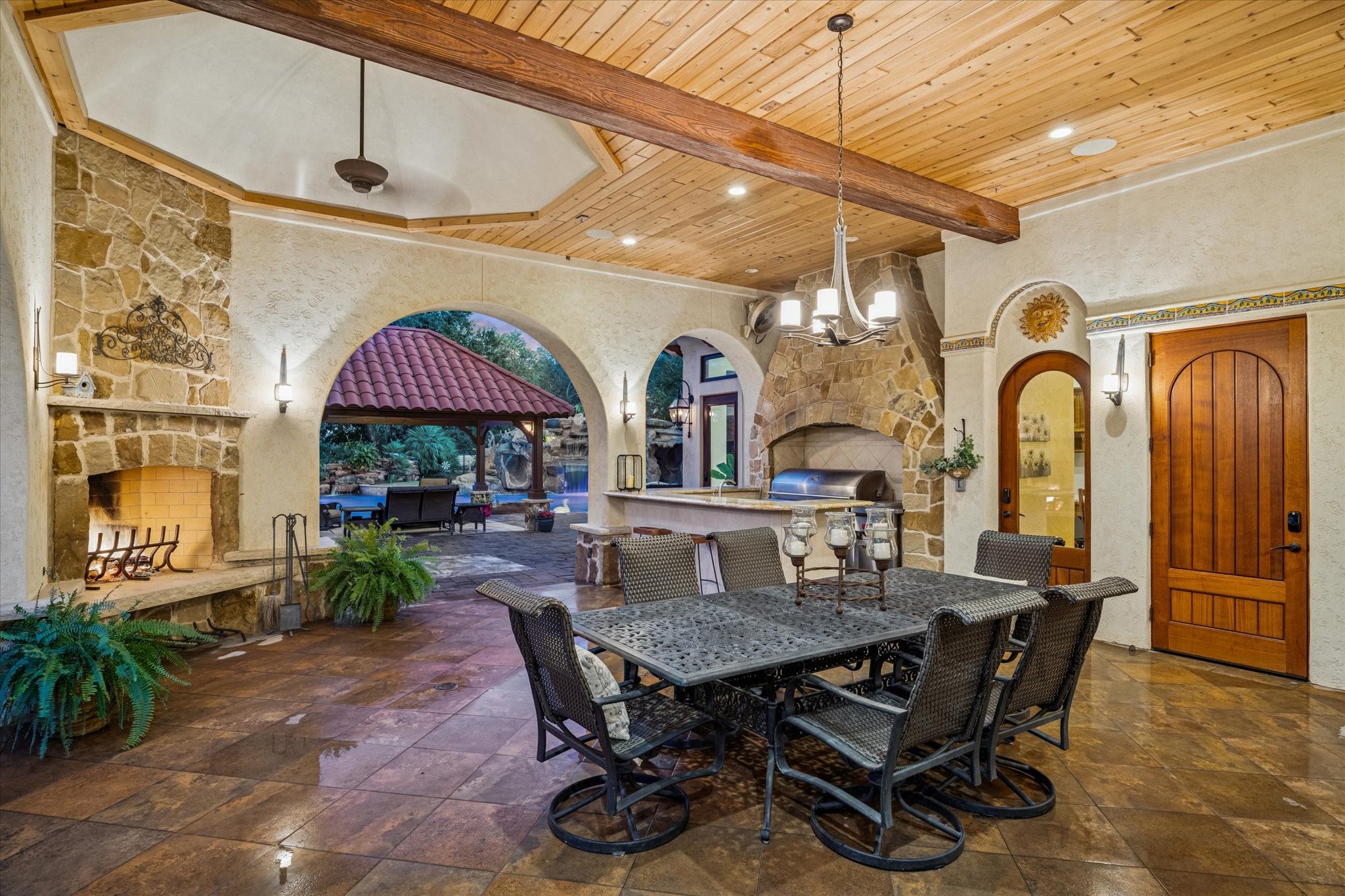 21538 Mueschke Road Tomball, TX 77377 - Photo 45 of 50 Elegant outdoor living with timeless design! This covered patio features a soaring wood-beamed ceiling, stone fireplace, and built-in grill for year-round entertaining. Arched openings frame views of the lush backyard and resort-style pool. Perfect for dining al fresco or relaxing by the fire, this space blends comfort and sophistication.