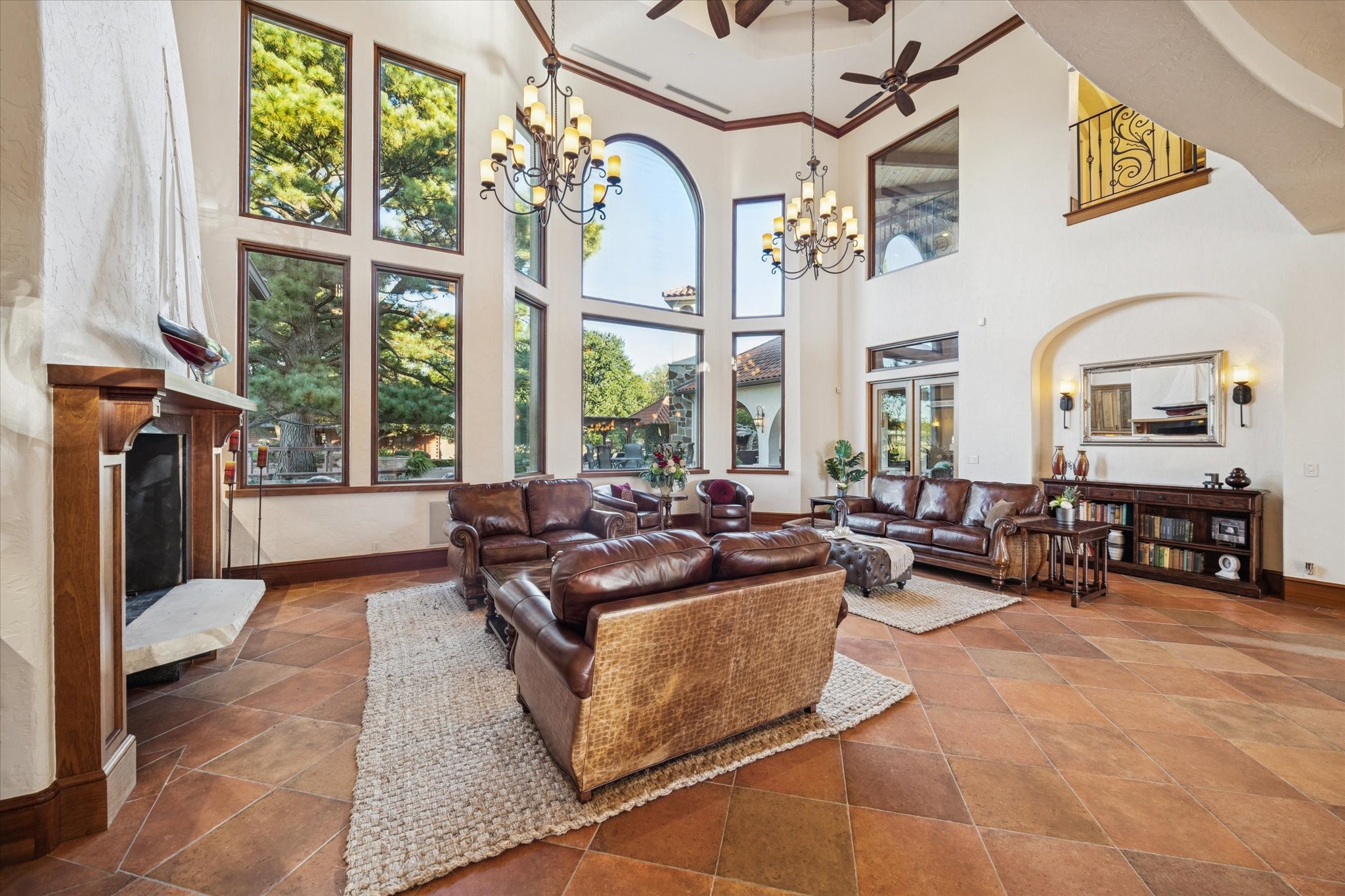 21538 Mueschke Road Tomball, TX 77377 - Photo 5 of 50 This impressive living room showcases soaring ceilings and a wall of oversized windows that fill the space with natural light. Elegant chandeliers and a grand fireplace create a warm yet luxurious atmosphere. The open design offers seamless flow for entertaining while highlighting stunning architectural details. Enjoy breathtaking views of the lush outdoor surroundings from every angle.