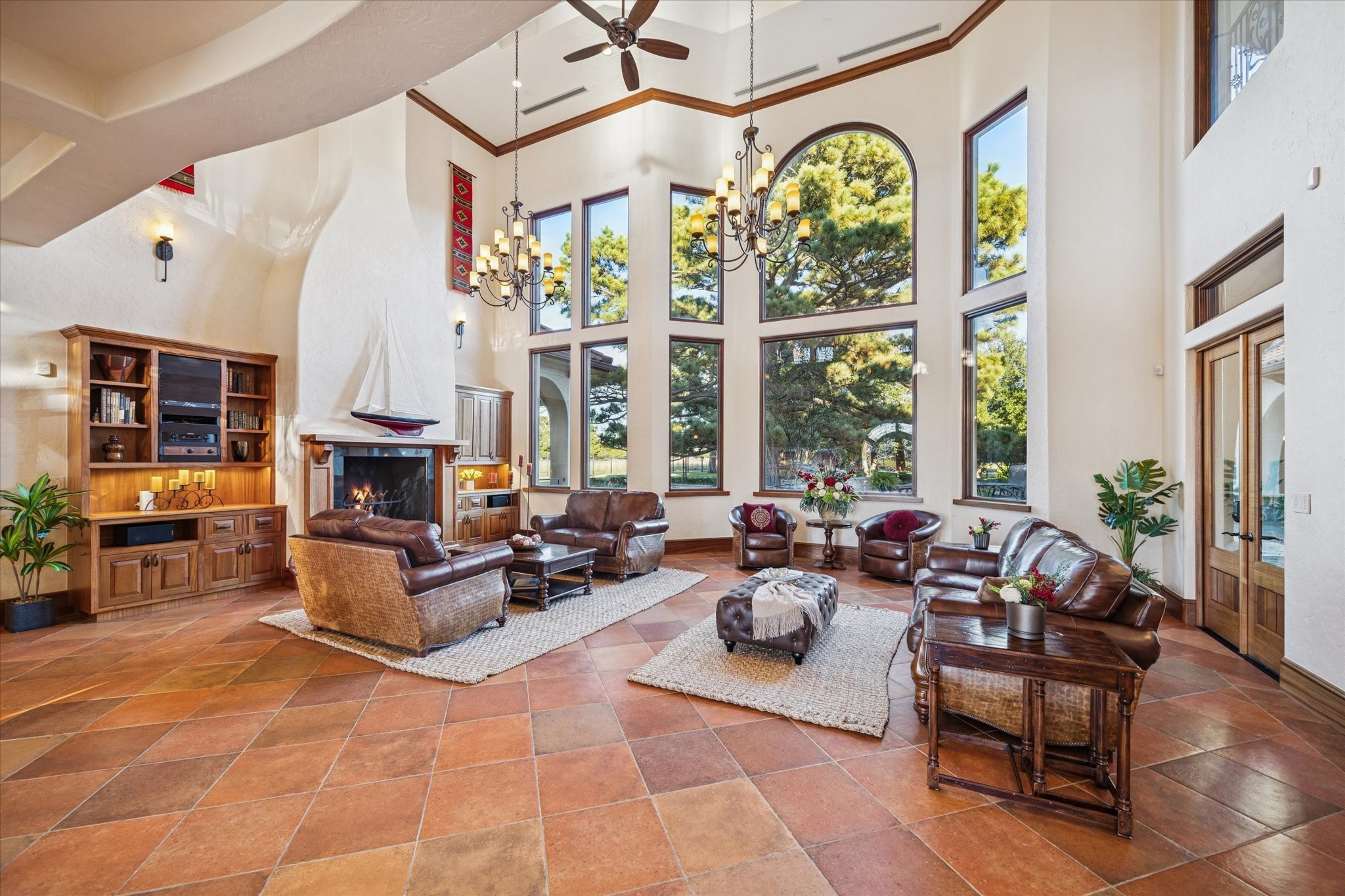 21538 Mueschke Road Tomball, TX 77377 - Photo 6 of 50 This grand formal living room, just beyond the entry, features a 26" ceiling, coffered wood-beam ceilings, two oversized wrought-iron chandeliers, and Mediterranean architectural details. A raised wood-burning fireplace with chiseled stone hearth and built-ins creates a stunning focal point, while abundant natural light and mahogany accents evoke an elegant hacienda-style retreat.