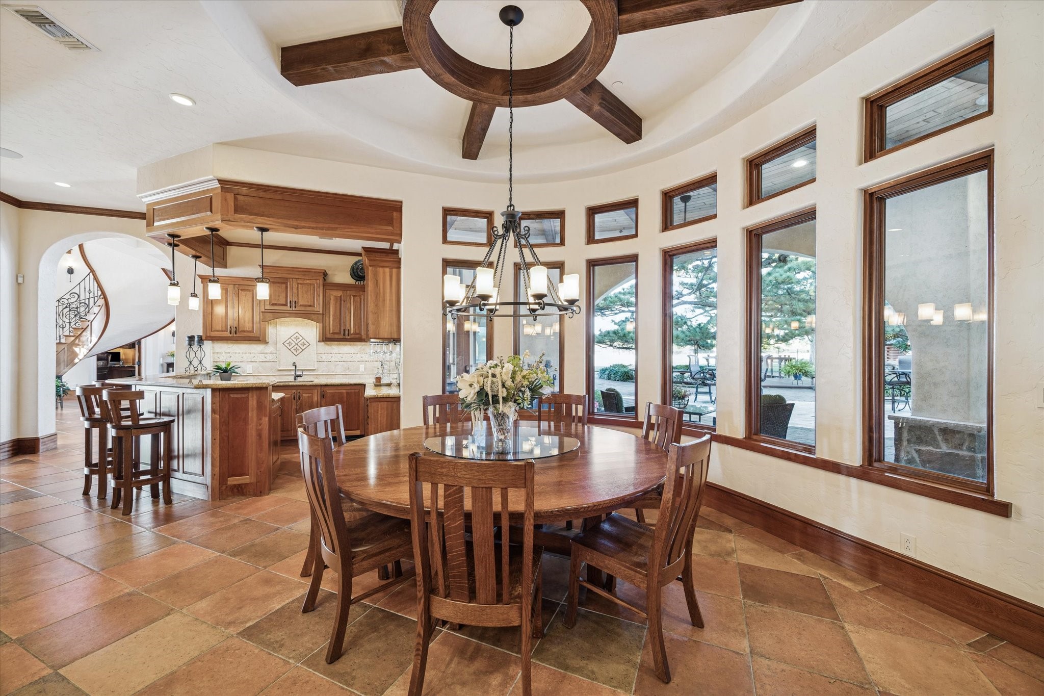21538 Mueschke Road Tomball, TX 77377 - Photo 7 of 50 Spacious breakfast area with an adjacent full bar. The bar features space for stools, a sink, Sub-Zero ice maker, California ice chest, glass-front display cabinetry, liquor shelving, and a wine glass rack, ideal for entertaining and enjoying quality time with loved ones. Multiple large windows showcase stunning views of the patio and pool, while the circular wood-beam ceiling adds a distinctive Hacienda-Mediterranean touch to this beautiful space.