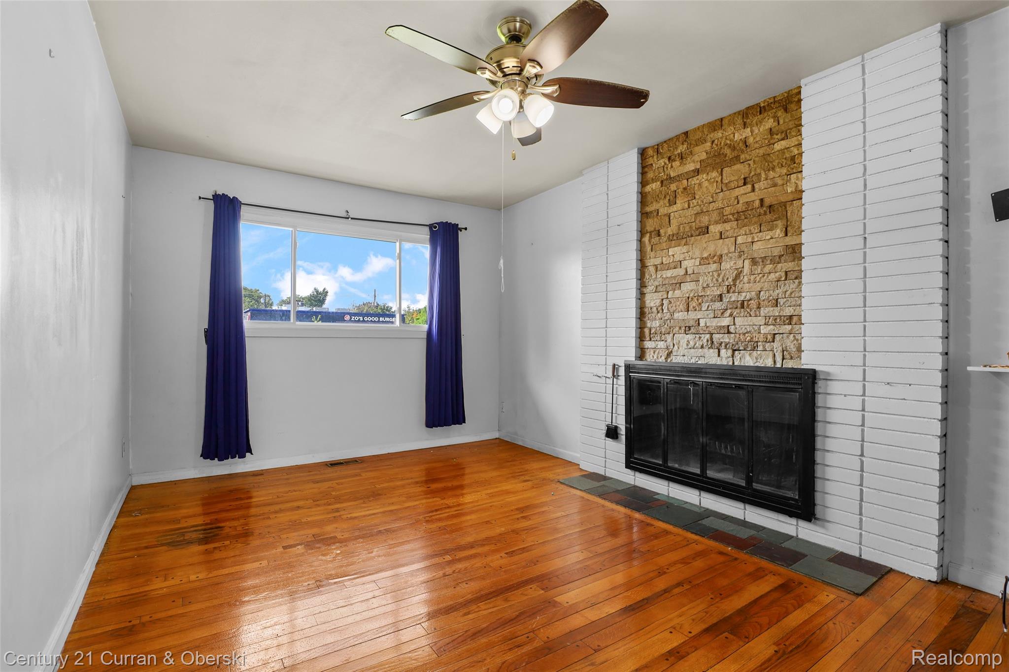 704 Inkster Road Dearborn Heights, MI 48127 - Photo 13 of 32 Hardwood flooring, brick fireplace with stone veneer accent, ceiling fan with integrated lighting, and a large window providing natural light