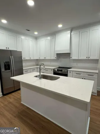 a kitchen with stainless steel appliances granite countertop a sink a stove a refrigerator a microwave oven with white cabinets and wooden floor