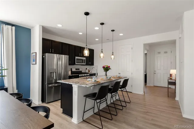 a kitchen with stainless steel appliances kitchen island granite countertop a refrigerator a stove a sink dishwasher and a dining table with wooden floor