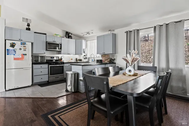 a kitchen with stainless steel appliances granite countertop a stove a refrigerator a sink a dining table and chairs