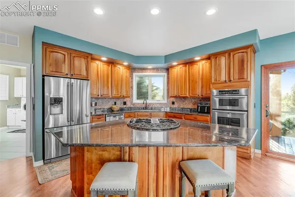 a kitchen with stainless steel appliances granite countertop a stove a refrigerator a sink a dining table and chairs with wooden floor